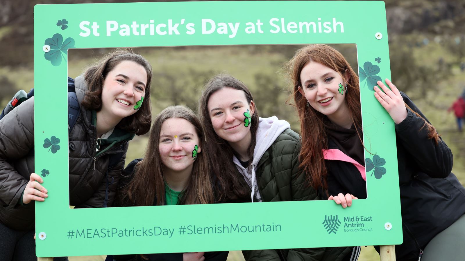 A group of girls on Slemish mountain, holding a novelty St. Patrick's Day themed frame for a photo.